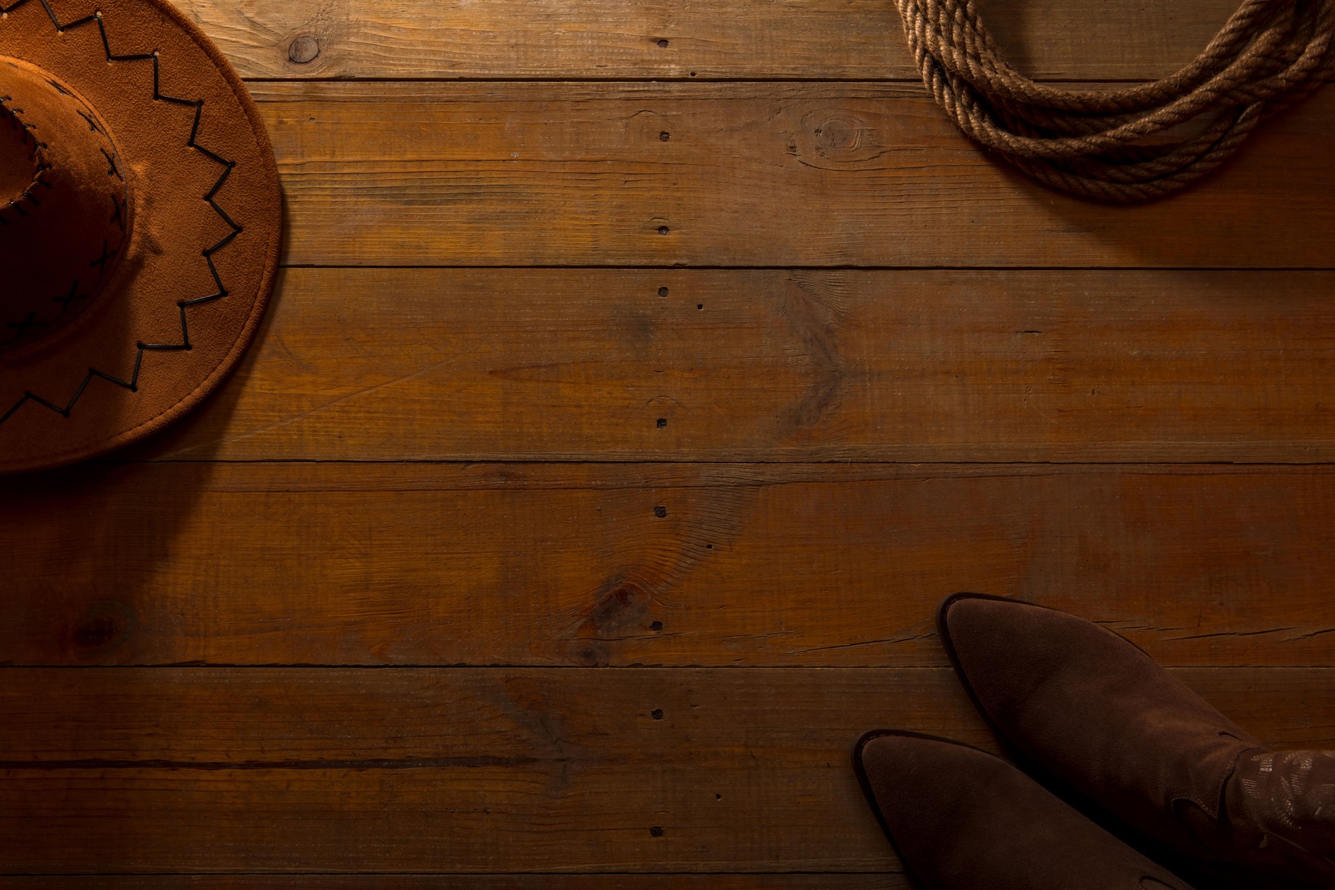 Cowboy hat and boots with a rope on a barn wood background